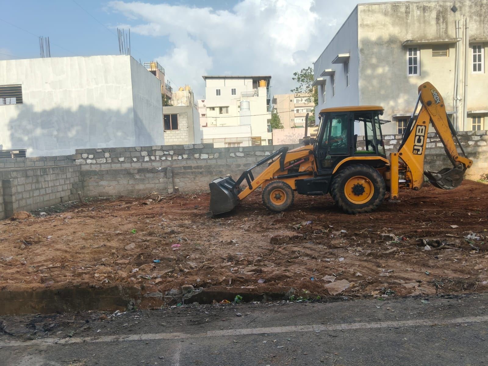 Excavator clearing debris and overgrowth on a vacant plot
